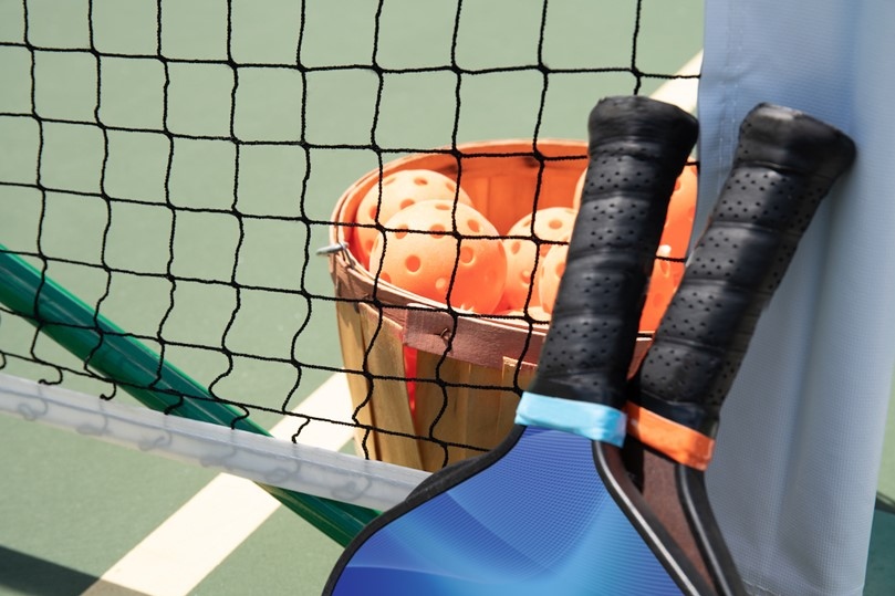 Bucket of pickleballs sits next to rackets